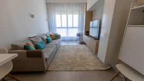A modern living room with a sofa, TV, and a dining area. - Apto Confort vel com Linda Vista Frente Para o mar (Santos)