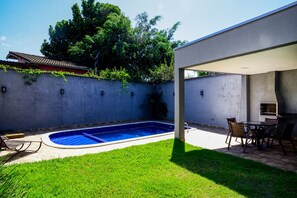 Ein Garten mit Pool, überdachter Terrasse und Grill.