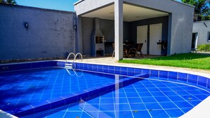 Una piscina con deck de baldosas, un patio cubierto y una parrilla para barbacoa.
