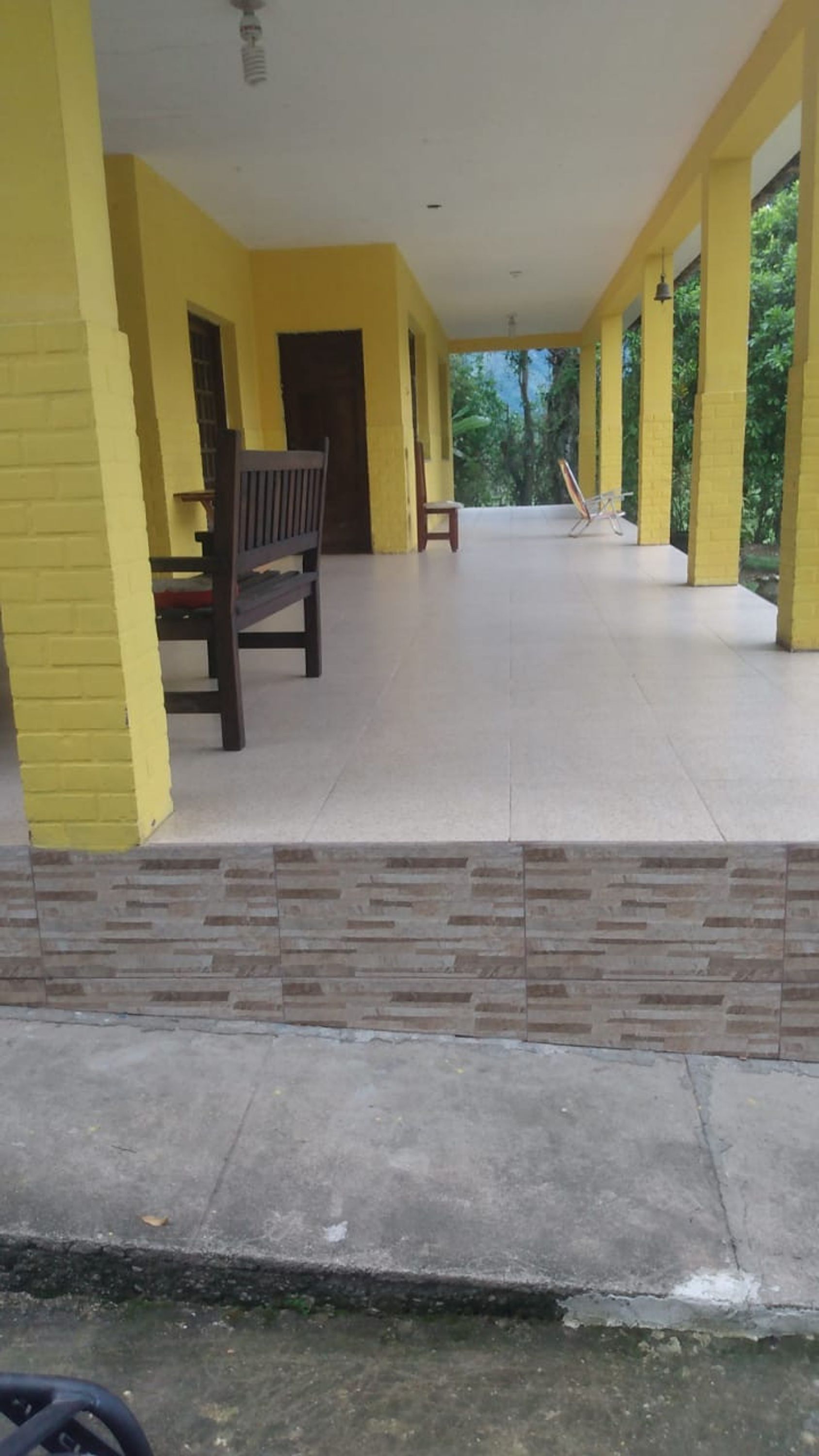 A covered outdoor area with yellow walls and a tiled floor, featuring a bench and a door.