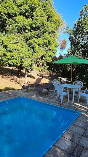 A swimming pool with lounge chairs and an umbrella. - Casa de Campo com Churrasq e Wifi em Mag RJ (Mage)