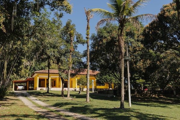 A yellow house with a red roof surrounded by trees and a clear sky. - Casa de Campo com Churrasq e Wifi em Mag RJ (Mage)
