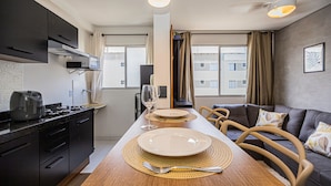 A modern kitchen with dark cabinets, a wooden dining table set with plates, a coffee maker, and a wine glass. - Confort vel Apartamento com Wi-fi pet Friendly (Sorocaba)