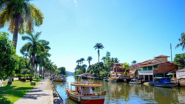 Un canal où naviguent des bateaux, une promenade dallée et des palmiers.