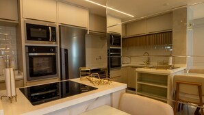 A modern kitchen with built-in appliances, a central island, and a dining area with a chair. - Apto Confort vel com Wi-fi e Churrasqueira (Fortaleza)