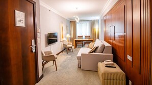 Une chambre d’hôtel avec une porte en bois, une télévision, un canapé, une petite table et une fenêtre avec des rideaux.