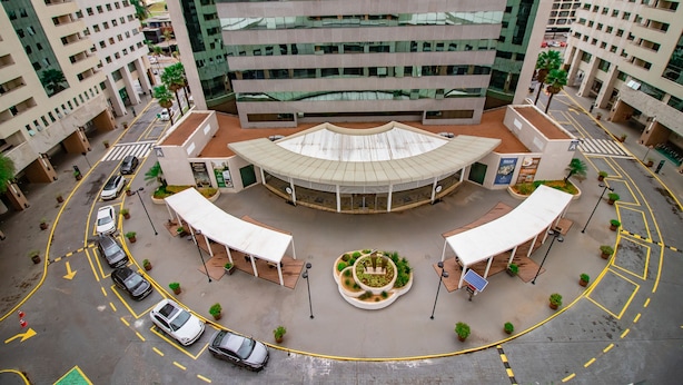 Un parking à plusieurs niveaux doté d’une place centrale circulaire, entouré de bâtiments modernes aux façades vitrées réfléchissantes.