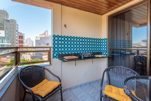 A balcony with wicker chairs, a tiled backsplash, and a view of the cityscape. - Apto Confort vel a 450m do mar da Praia do Morro (Guarapari)