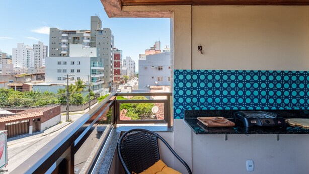 A balcony with a view of a cityscape, a wicker chair, and a kitchen area with a toaster. - Apto Confort vel a 450m do mar da Praia do Morro (Guarapari)