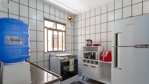 A kitchen with white tiled walls, a gas stove, a microwave, a refrigerator, and a large blue water dispenser. - Apto Confort vel a 450m do mar da Praia do Morro (Guarapari)