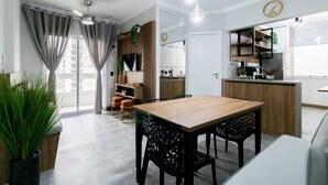 A modern kitchen with a wooden countertop, a built-in oven, and a sink. There is a dining area with a wooden table and black chairs. - Apto a 500m da Praia Canto do Forte - Praia Grande (Praia Grande)