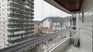 A balcony with a view of a cityscape, including a tall building under construction and other buildings in the background. - Apto a 500m da Praia Canto do Forte - Praia Grande (Praia Grande)