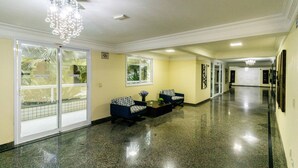 A spacious hallway with two sofas and a coffee table, a chandelier, and a door with a glass panel. - Apto a 500m da Praia Canto do Forte - Praia Grande (Praia Grande)