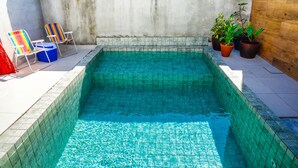 A swimming pool with tiled walls, two lounge chairs, and potted plants. - Chal com Piscina e Churrasq em Caraguatatuba SP (Caraguatatuba)