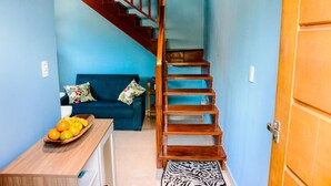 A staircase leading to a second floor, a blue sofa with floral cushions, and a wooden table with fruit. - Chal com Piscina e Churrasq em Caraguatatuba SP (Caraguatatuba)
