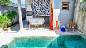 A swimming pool with tiled steps, a table with chairs, and a small window. - Chal com Piscina e Churrasq em Caraguatatuba SP (Caraguatatuba)