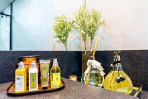 Una encimera de baño con varios artículos de aseo y un florero con flores.