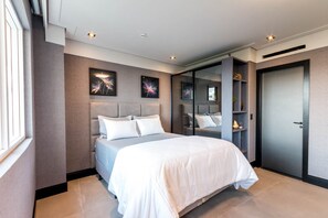 A modern bedroom with a large bed, a built-in wardrobe, and artwork on the walls.
