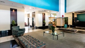 Un hall d’hôtel au design moderne, comprenant un espace salon avec un canapé et des fauteuils, une table basse en verre et un comptoir d’accueil.