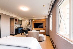 Ett modernt hotellrum med en stor säng, ett skrivbord, en stol, en tv och ett fönster.