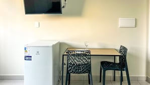 Uma cozinha compacta equipada com geladeira, uma mesa pequena, duas cadeiras e uma TV de tela plana presa na parede.