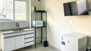 Uma cozinha com bancada de granito, armários brancos, micro-ondas, geladeira compacta, TV fixada na parede e janela com vista para o exterior.