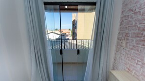 A balcony with a glass door, white curtains, and a brick wall. - Apto com Ar-condicionado a 350m do mar em Aracaju (Aracaju)