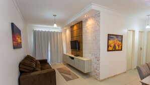 A modern living room with a brown sofa, a TV mounted on a brick wall, and a dining area with a table and chairs. - Apto com Ar-condicionado a 350m do mar em Aracaju (Aracaju)