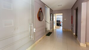 A hallway with a door on the left, a mirror on the wall, and a car parked in the distance. - Apto com Ar-condicionado a 350m do mar em Aracaju (Aracaju)