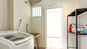 A laundry area with a washing machine, a small window, and a shelf with cleaning supplies. - Loft p Home Office com Wifi em Sorocaba SP (Sorocaba)