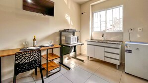 A compact kitchen with a dining table, chairs, a microwave, a refrigerator, and a TV mounted on the wall. - Loft p Home Office com Wifi em Sorocaba SP (Sorocaba)
