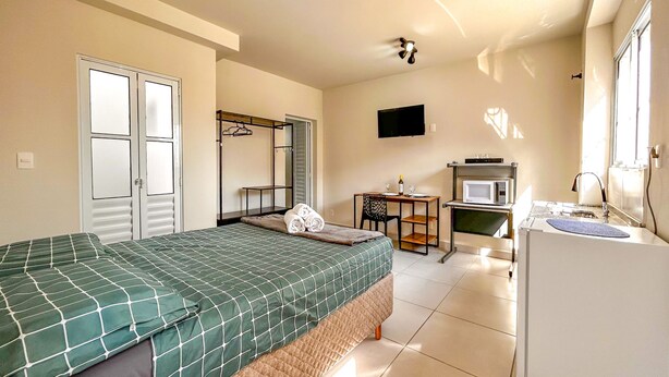 A hotel room with a bed, a desk with a chair, a TV, a microwave, and a window. - Loft p Home Office com Wifi em Sorocaba SP (Sorocaba)