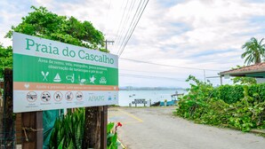A sign for Praia do Cascalho, a natural area for swimming, fishing, and sunbathing, with a view of the sea and a boat dock. - Apto pr Ximo do mar e do Beto Carrero World (Penha)