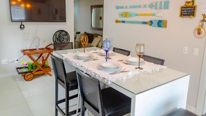 A dining area with a glass table set for four, a TV mounted on the wall, and paddleboard decorations. - Apto pr Ximo do mar e do Beto Carrero World (Penha)