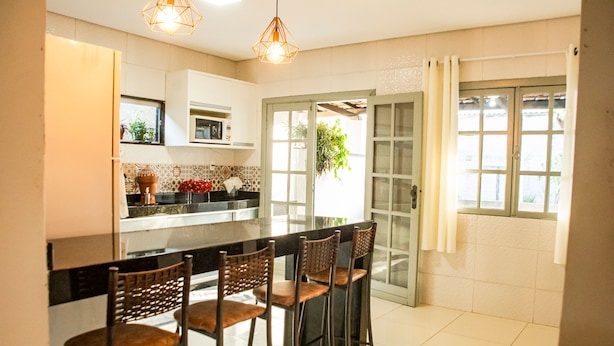A modern kitchen with a central island, bar stools, and a view through a glass door to the outside. - Casa c Tima Localiza o em Teixeira de Freitas-ba (Teixeira de Freitas)