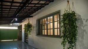 A hallway with a green door, a window with a wooden frame, and hanging plants. - Casa c Tima Localiza o em Teixeira de Freitas-ba (Teixeira de Freitas)