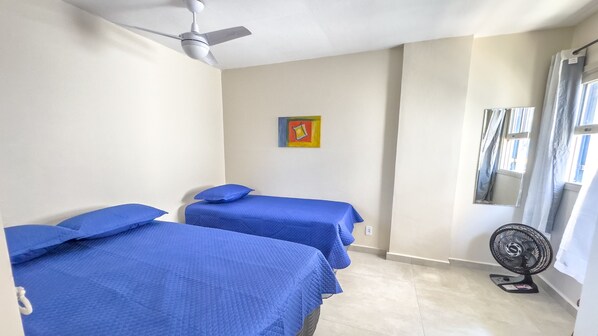 A room with two beds, a ceiling fan, a window with curtains, and a wall-mounted air conditioner. - Aconchegante e Espa oso Apto c Piscina e Churrasq (Cabo Frio)