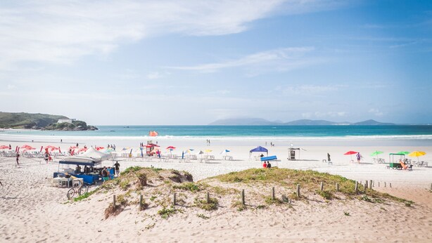 A beach with umbrellas, beach chairs, and a dune. - Aconchegante e Espa oso Apto c Piscina e Churrasq (Cabo Frio)