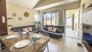 A dining area with a table set for two, a sofa, and a potted plant. - Aconchegante e Espa oso Apto c Piscina e Churrasq (Cabo Frio)