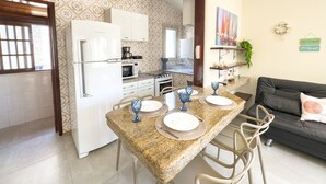 A modern kitchen with white appliances, a dining table set with plates and glasses, and a living area with a sofa and decorative pillows. - Aconchegante e Espa oso Apto c Piscina e Churrasq (Cabo Frio)