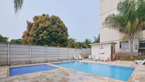 A swimming pool with tiled flooring and white lounge chairs. - Flat Confort vel com Wi-fi em Santa Cruz RJ (Rio de Janeiro)