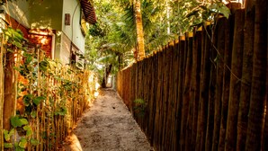 Un estrecho callejón con una valla de madera a un lado y un muro de ladrillo al otro, que conduce a la entrada de un edificio.