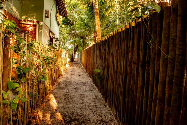 A narrow alleyway with a wooden fence on one side and a brick wall on the other, leading to a building entrance.