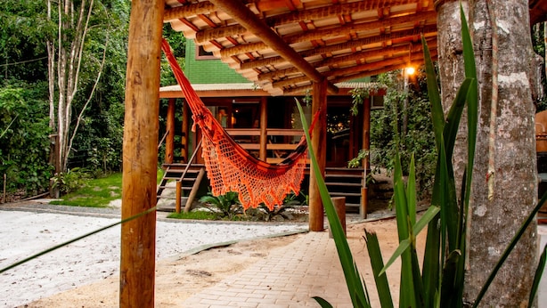 A wooden structure with a hammock, surrounded by greenery and a paved area. - Suite Recanto dos Macacos - Quarto 2 (Prado)