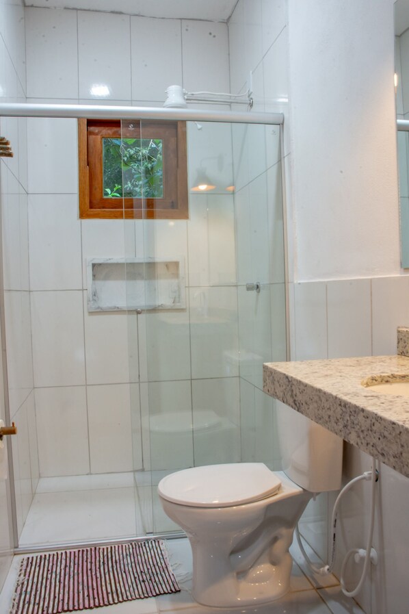 Un baño con cabina de ducha de vidrio, inodoro y tocador con encimera.