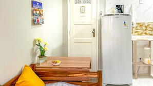 A compact kitchen with a white refrigerator, a wooden table with a bowl and flowers, and a door with a sticker. - Timo Studio c Wifi a 190m da Praia do Leme RJ (Rio de Janeiro)