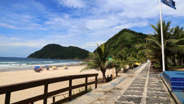 A beach with a wooden walkway, palm trees, and a flag on a pole. - Timo Apto c Wifi a 700m da Praia do Tombo-guaruj (Guarujá)