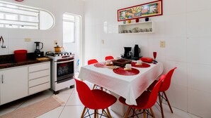 A modern kitchen with white cabinets, a stove, and a dining table with red chairs. - Timo Apto c Wifi a 700m da Praia do Tombo-guaruj (Guarujá)