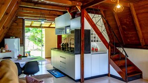 A compact kitchen with a dining area, wooden beams, and a staircase. - Charmoso Chal no Campo com Vista Para a Natureza (Sao Pedro de Alcantara)