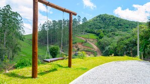 A wooden swing set in a grassy area with a view of a hilly landscape. - Charmoso Chal no Campo com Vista Para a Natureza (Sao Pedro de Alcantara)